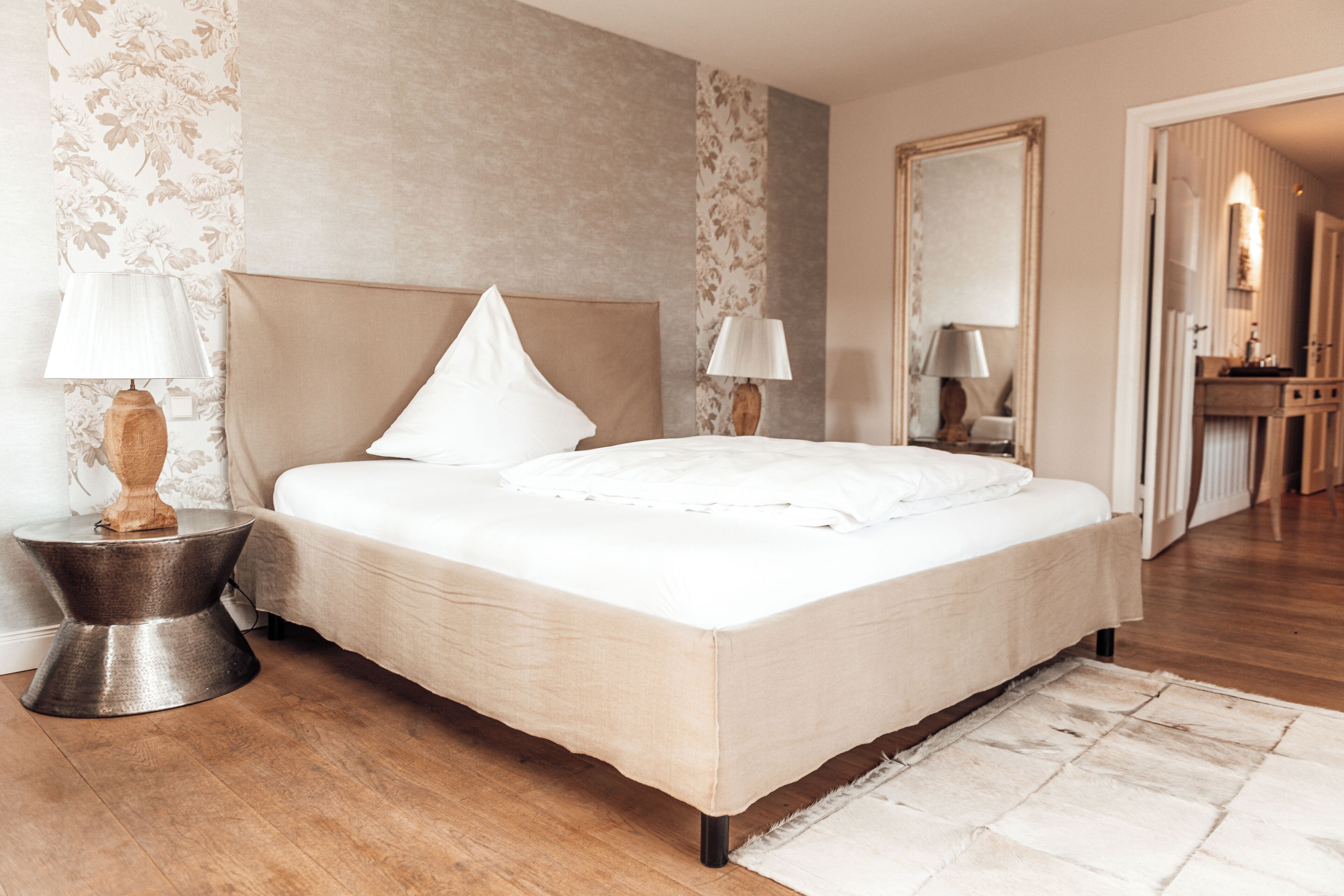 A neatly arranged bedroom with a large bed, two bedside lamps, and a mirror on the wall.