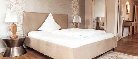 A neatly arranged bedroom with a large bed, two bedside lamps, and a mirror on the wall.