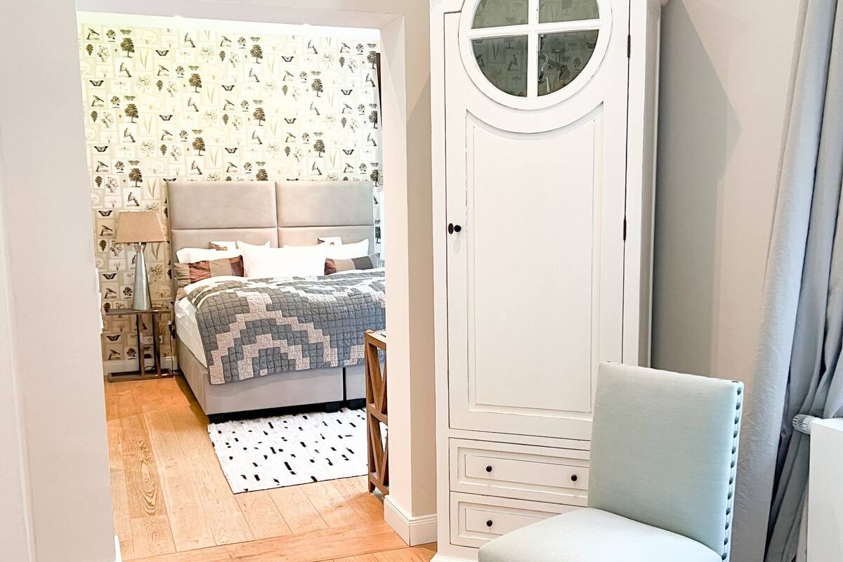 A bedroom with a bed, a wardrobe, a chair, and a patterned wallpaper.