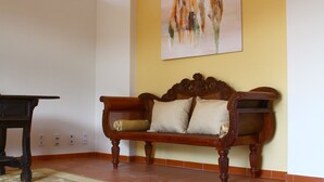 A wooden sofa with cushions against a yellow wall, a small table to the left, and a painting above. - Casa do Alfaro (Azambuja)