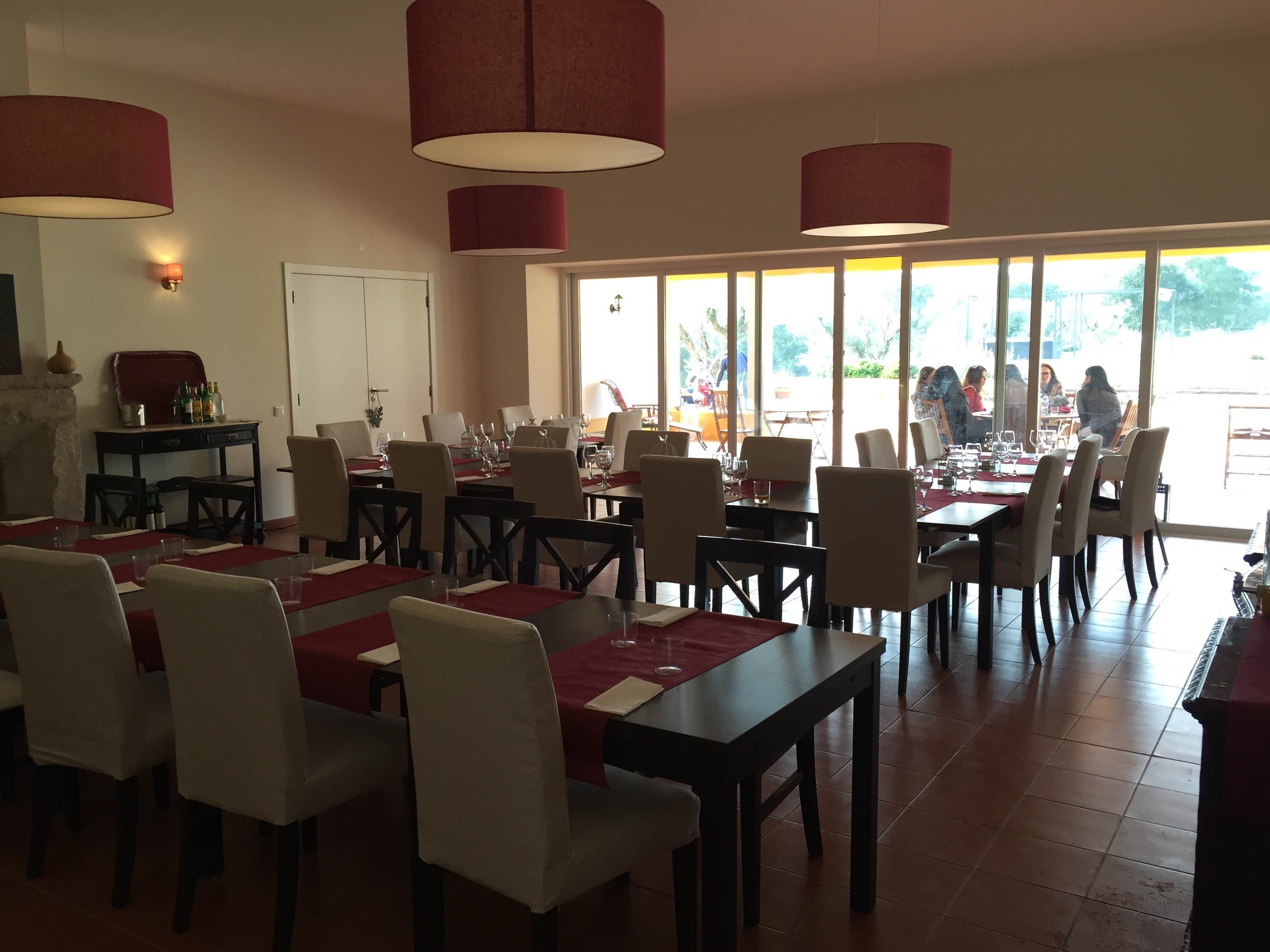 Un restaurante con mesas dispuestas para comer, amplias ventanas y lámparas rojas colgantes.