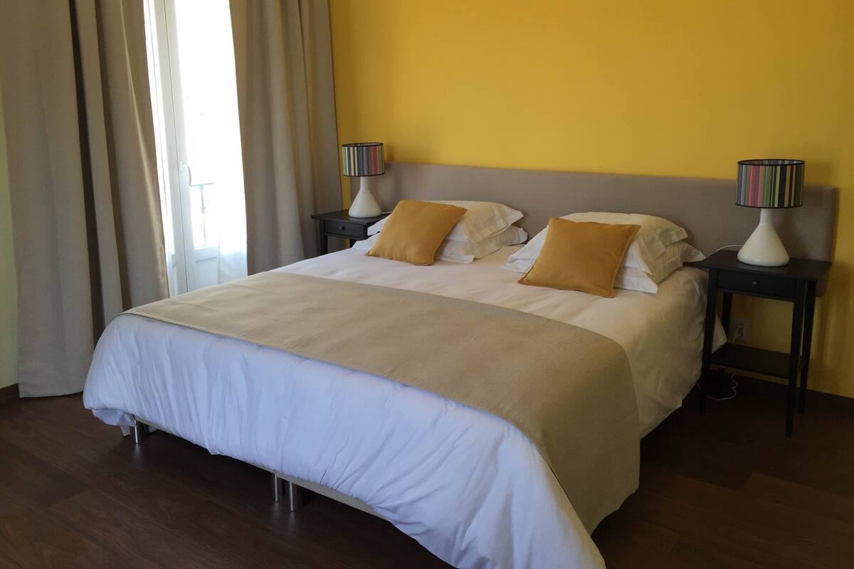 Una habitación de hotel con una cama grande, dos mesitas de noche y una ventana con cortinas.