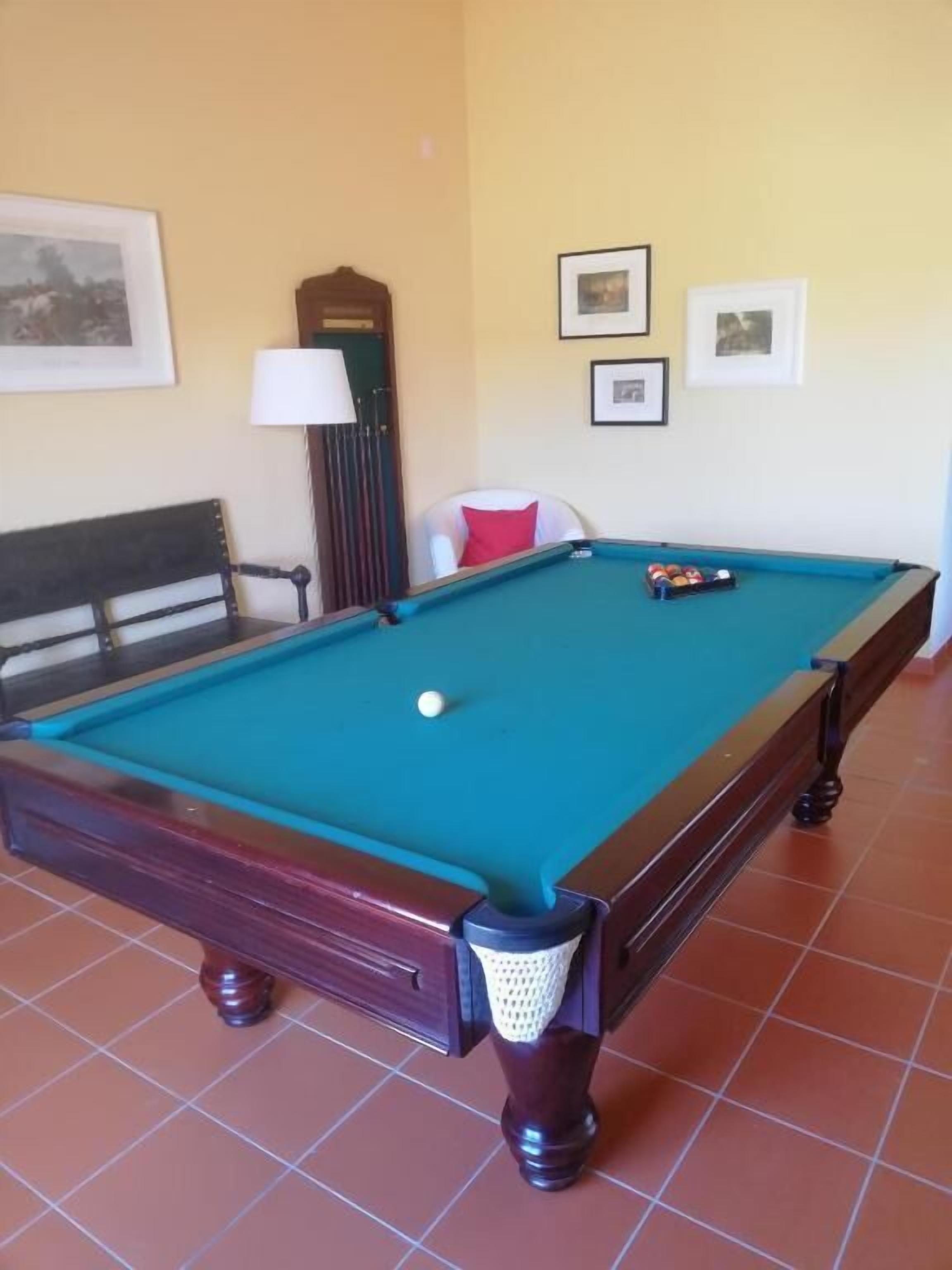 A pool table with balls, a lamp, and framed pictures on the wall.