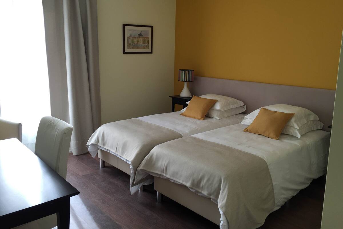 Una habitación de hotel con dos camas, un escritorio y una mesita de noche con una lámpara.