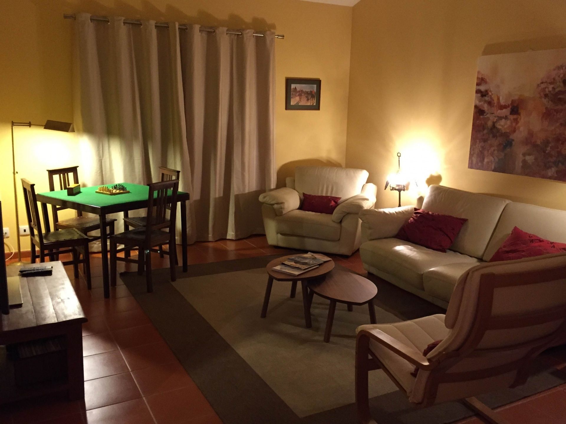 A living room with a sofa, armchairs, a coffee table, and a dining area with a chessboard.