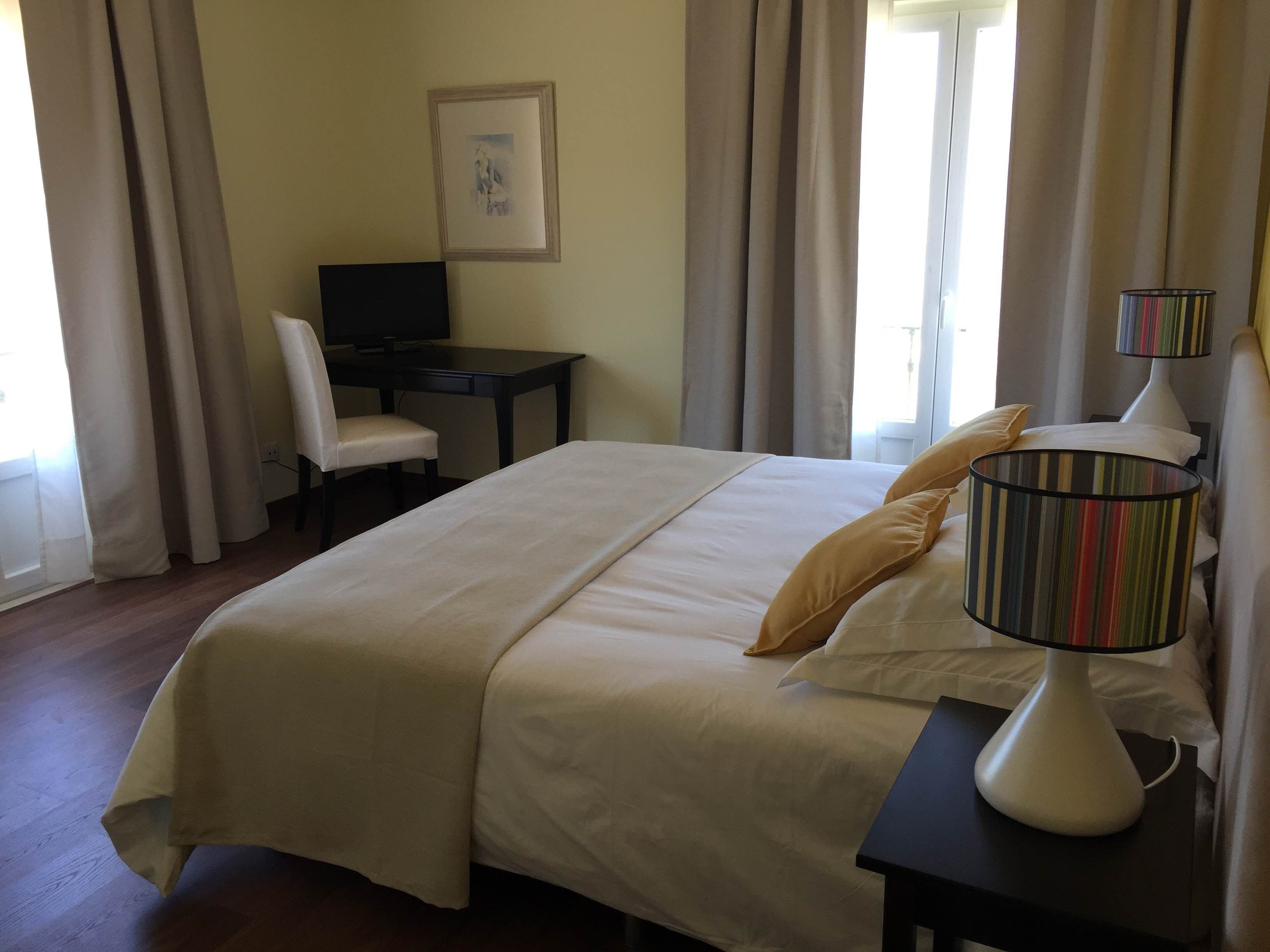 Habitación de hotel con una cama grande, un escritorio con silla, un televisor y una lámpara.