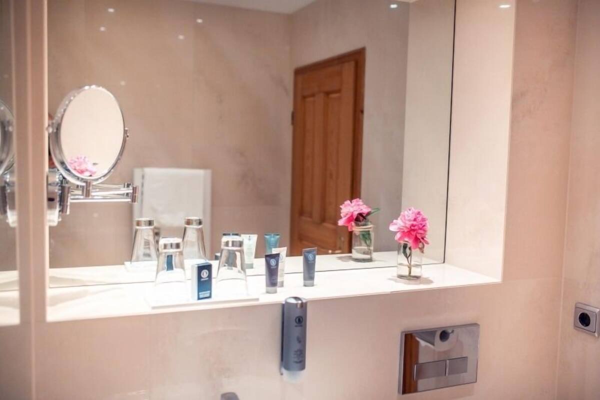 A bathroom with a large mirror, a sink, and a vanity with toiletries.
