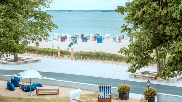 Eine Terrasse direkt am Strand mit Sitzgelegenheiten im Freien, Blick auf das Meer und einem Weg zum Strand.