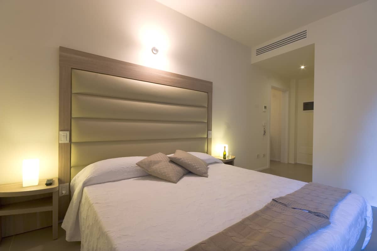 A neatly made bed with a headboard, a bedside table with a lamp, and a bottle of water.