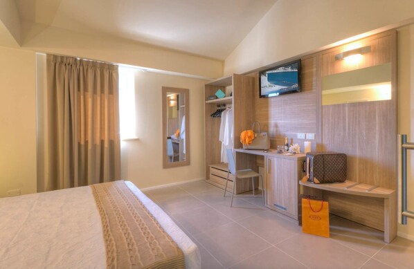 A hotel room with a bed, a desk with a chair, a TV mounted on the wall, and a wardrobe.