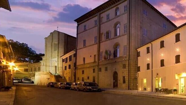 A hotel with multiple floors, a parking area, and a street view at dusk. - Palazzo Ruschioni Boutique Hotel (Camerano)