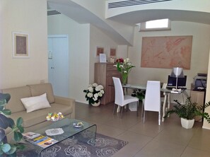 A modern living room with a glass coffee table, a beige sofa, and a dining area with a white table and chairs. - Palazzo Ruschioni Boutique Hotel (Camerano)