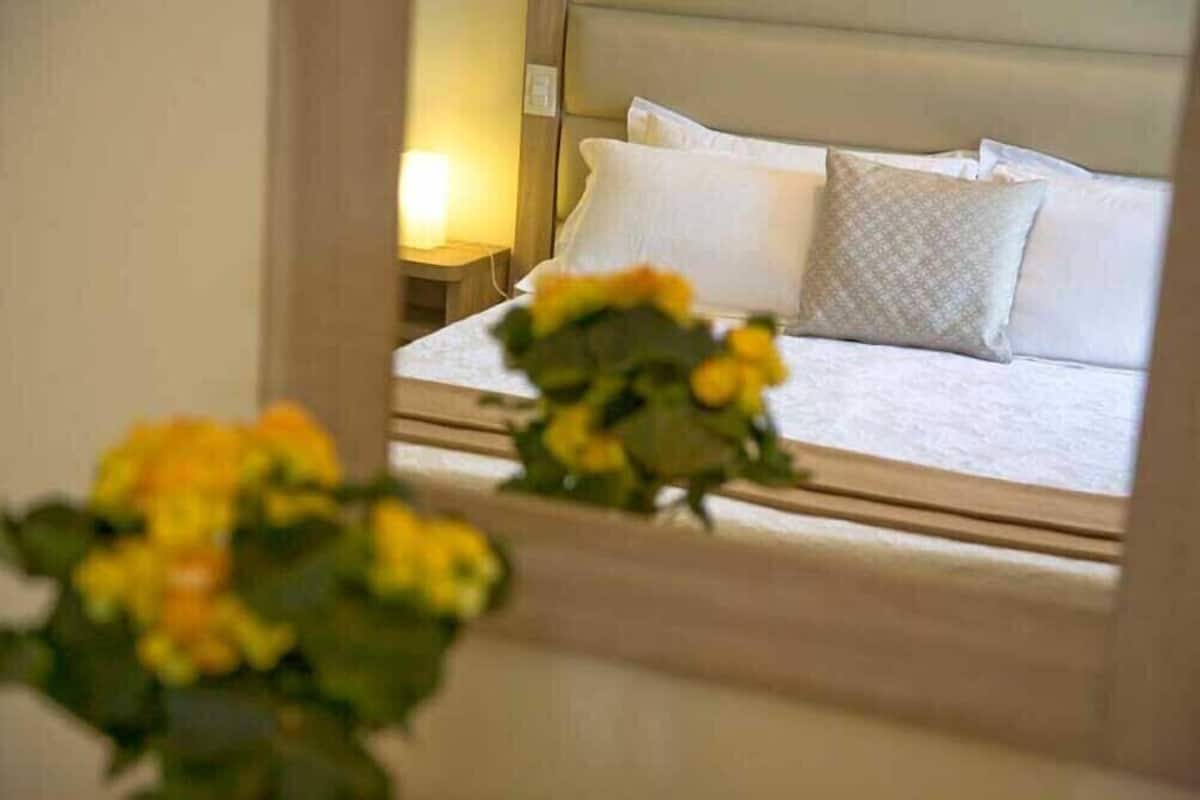 A hotel room with a bed, pillows, a nightstand, and a lamp.