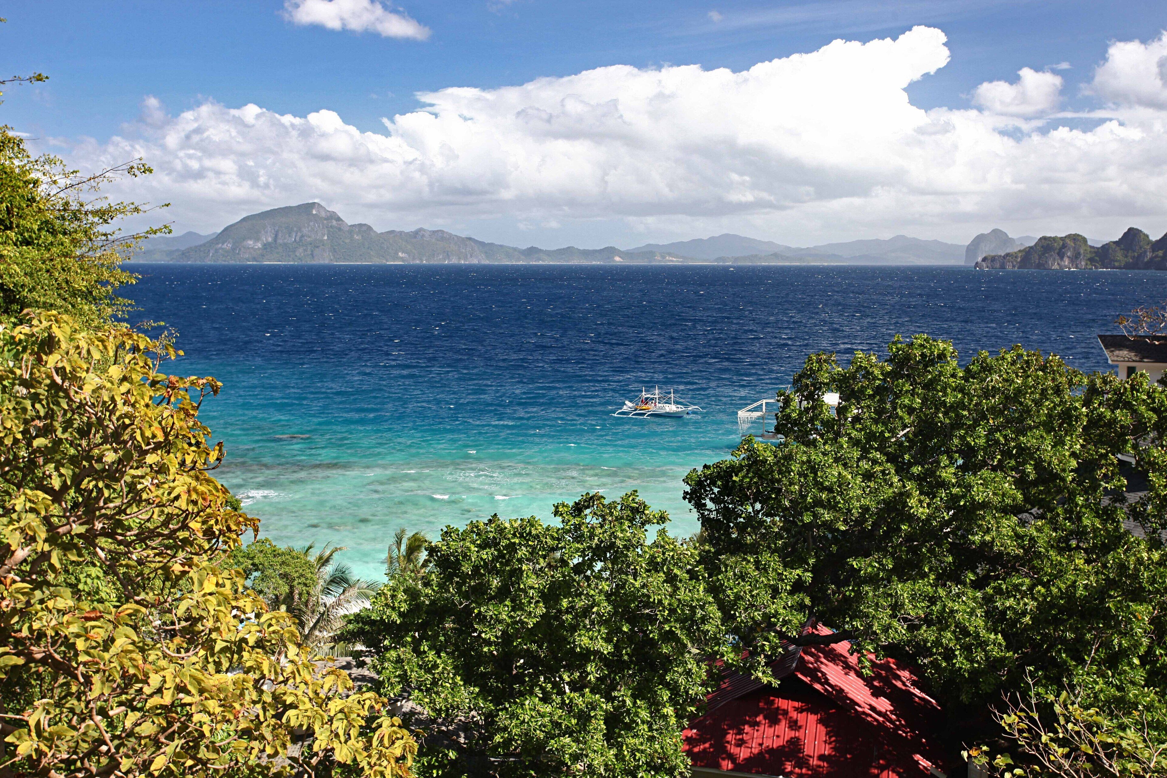 A coastal view with a boat, clear blue sea, and distant mountains.