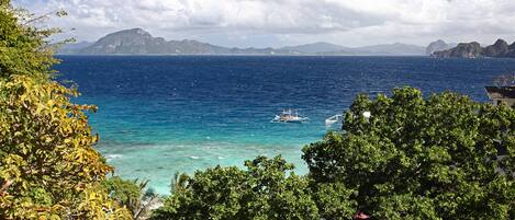 A coastal view with a boat, clear blue sea, and distant mountains.