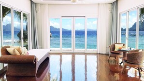 A spacious room with a large bed, a sitting area with a table, and a view of the ocean through large windows. - Matinloc Island Resort (El Nido)