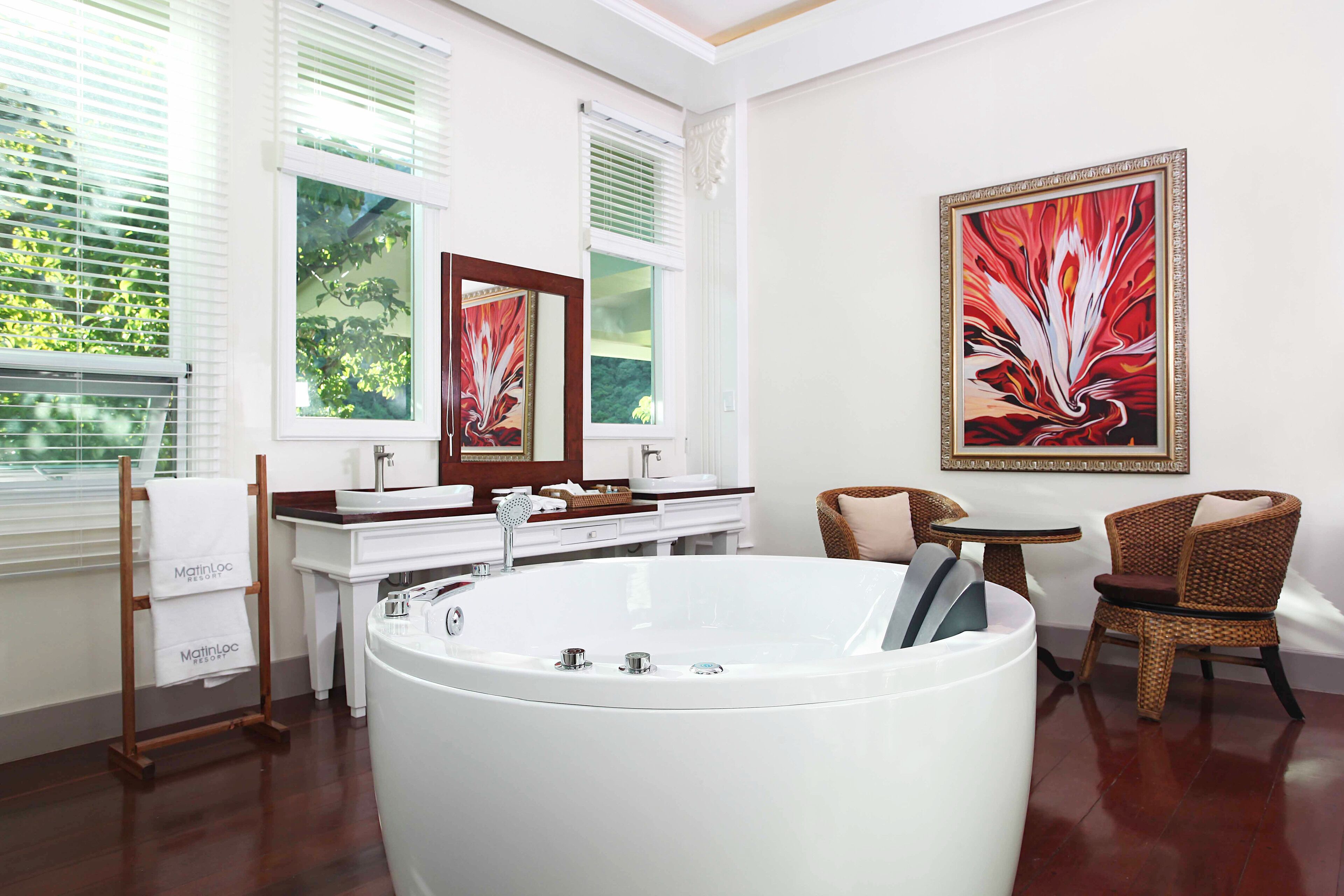 A modern bathroom with a freestanding bathtub, a vanity with a mirror, and wicker chairs.
