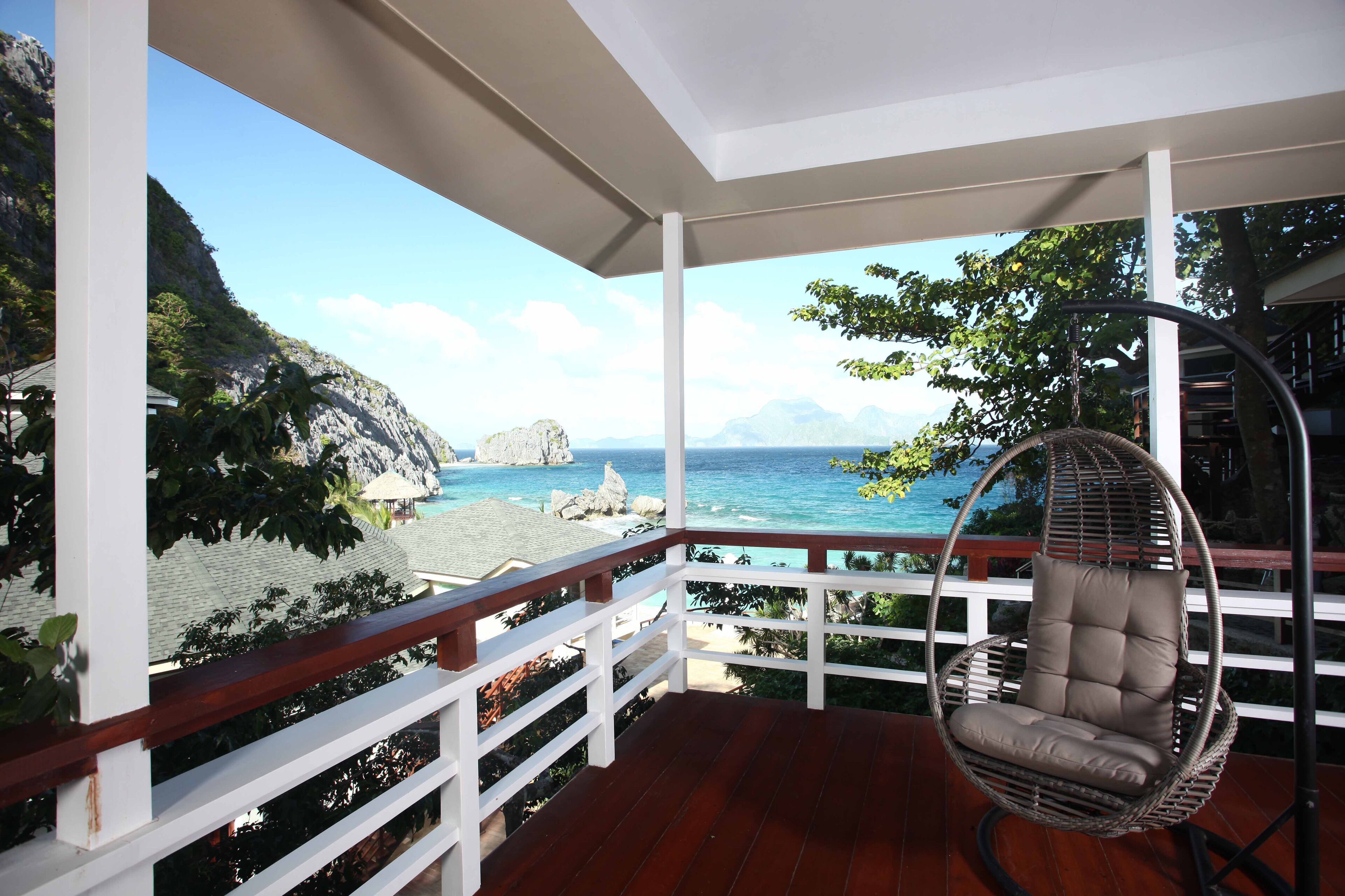 A wooden deck with a hanging chair overlooking a beach with rocky cliffs and the ocean.
