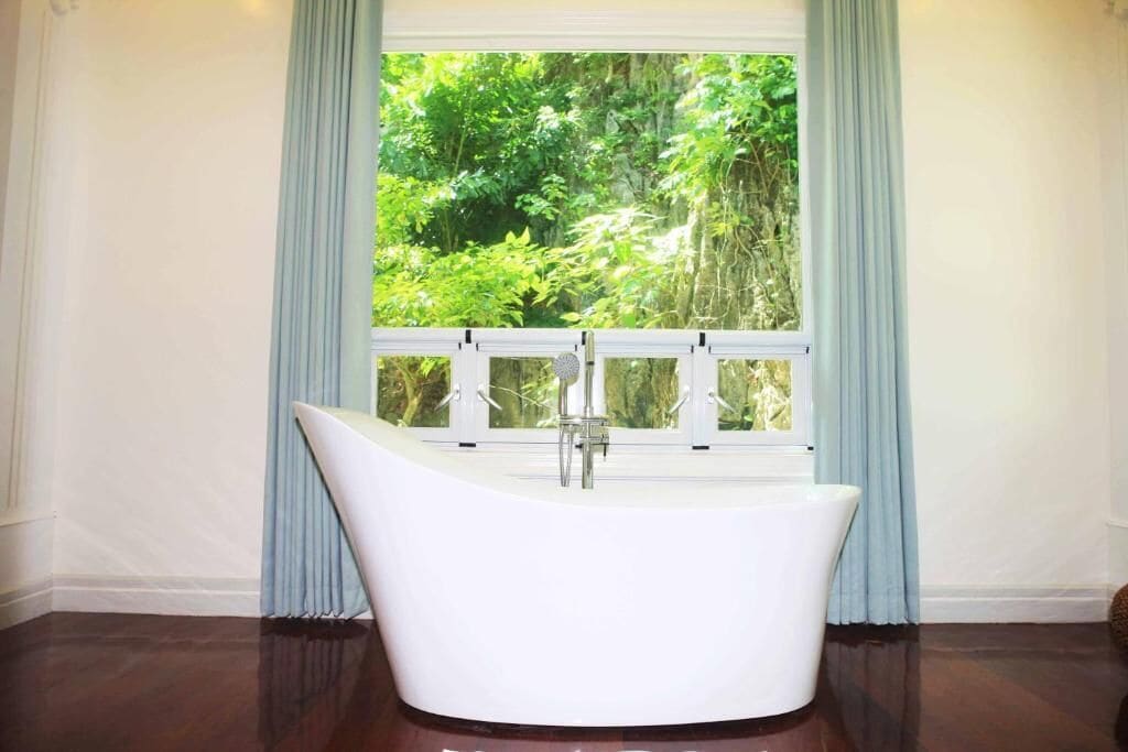 A freestanding bathtub in a room with a view of lush greenery through a window.
