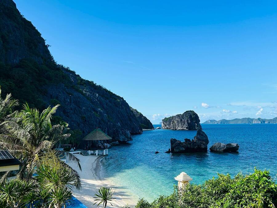 Un resort en la playa con piscina, palmeras y vistas al mar y las montañas.