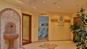 A lobby with a stone fountain, a tiled floor, a clock, and a staircase. - Pension Neururer (Soelden)