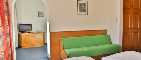 A hotel room with a wooden wardrobe, a green sofa, a bed with white bedding, and a television on a wooden cabinet.
