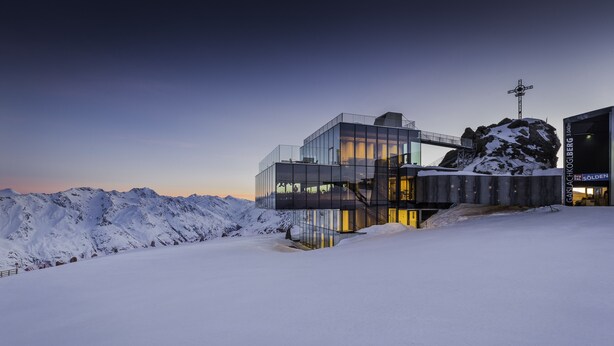 A modern glass building with a ski lift and snowy mountains in the background. - Pension Neururer (Soelden)