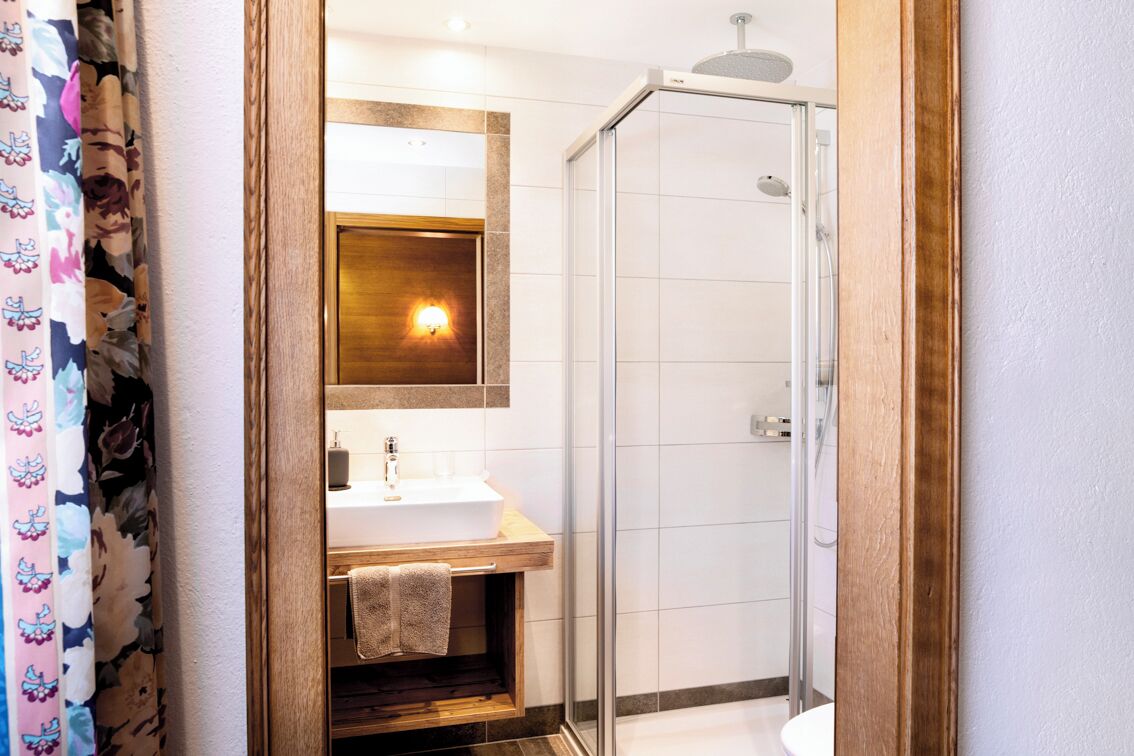 A bathroom with a wooden vanity, a white sink, a mirror, and a glass shower enclosure.