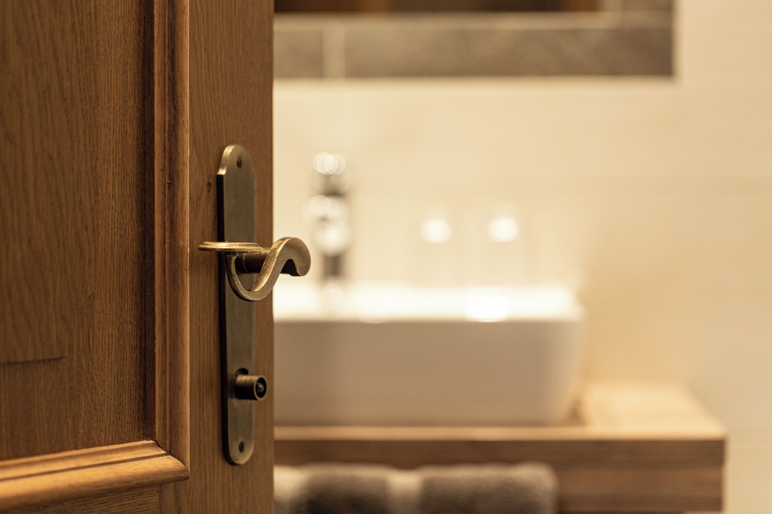 Una puerta de madera con un pomo moderno, que da acceso a un baño con un lavabo blanco y un perchero.