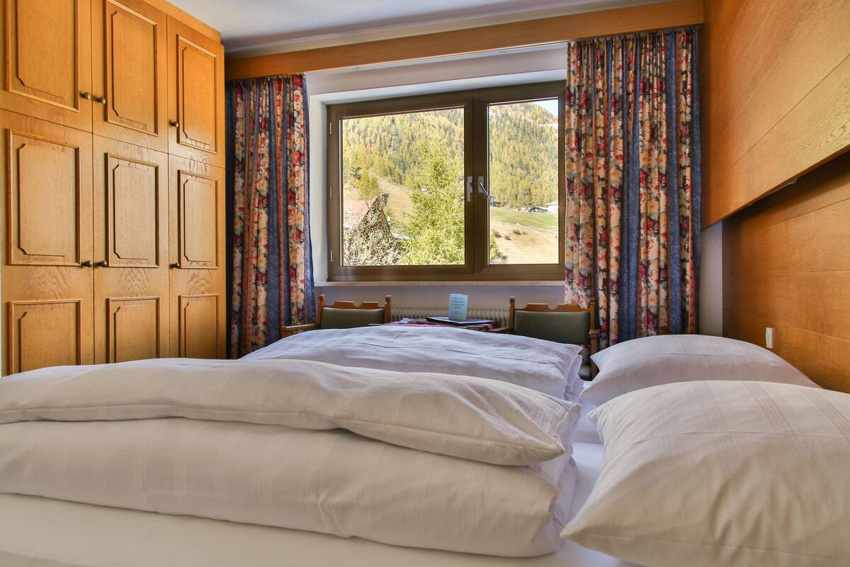 Habitación de hotel con una cama grande, armario de madera, escritorio con silla y ventana con cortinas.
