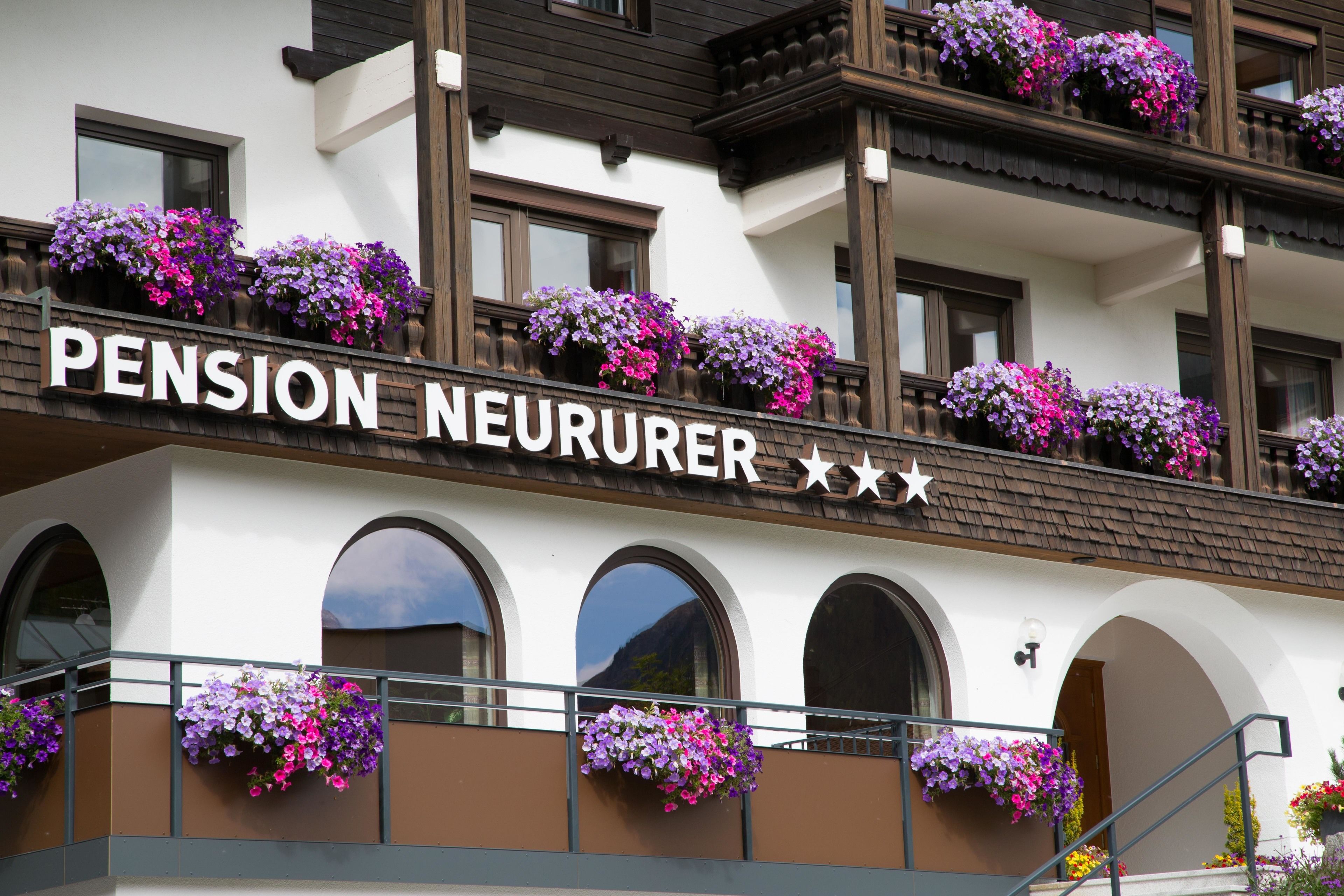 A building named "Pension Neururer" with balconies adorned with flower boxes.