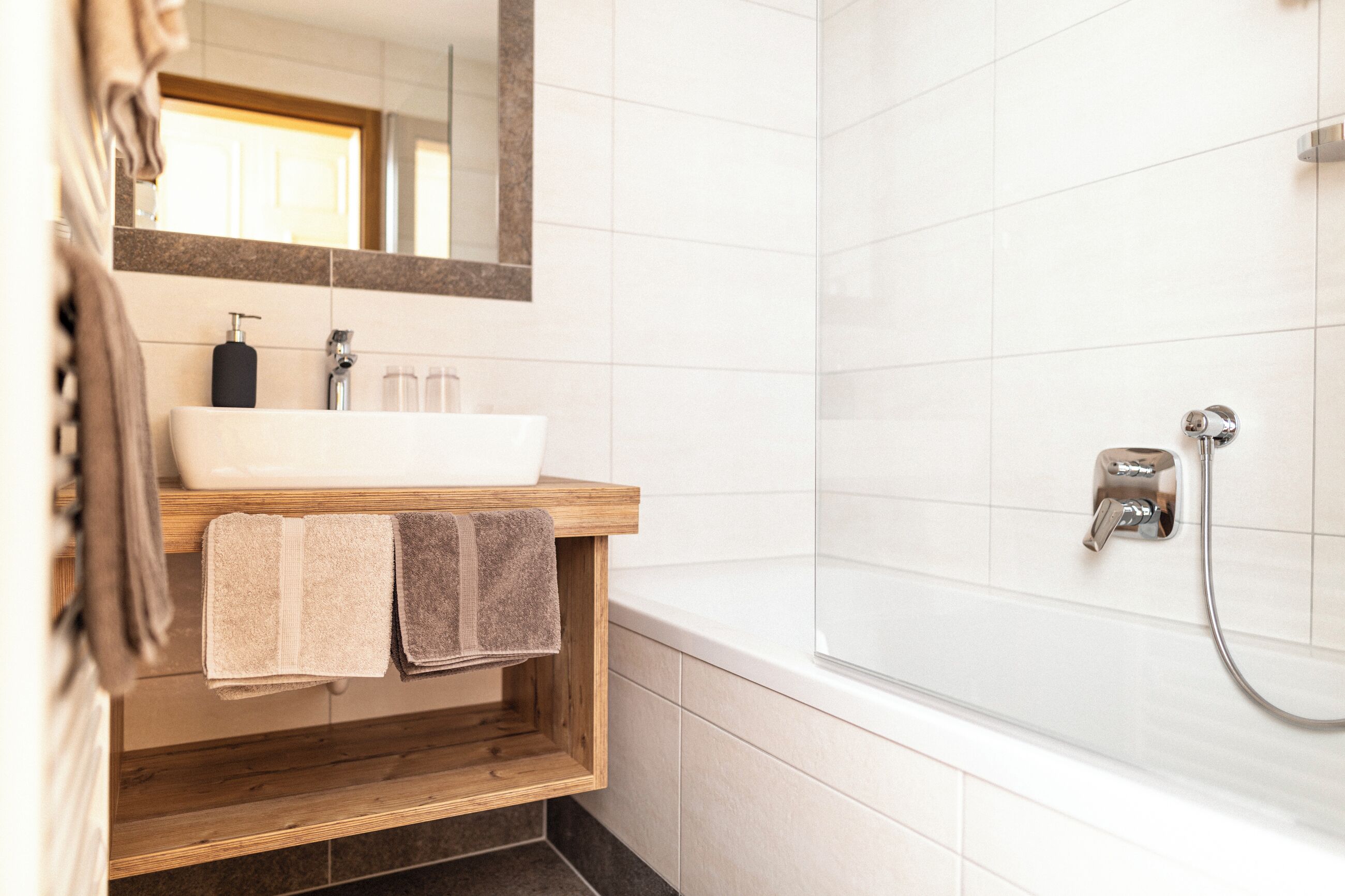 Un baño moderno con tocador de madera, lavabo blanco y un espejo grande.