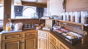 A kitchen with wooden cabinets, a buffet setup, and a window with curtains. - Pension Neururer (Soelden)