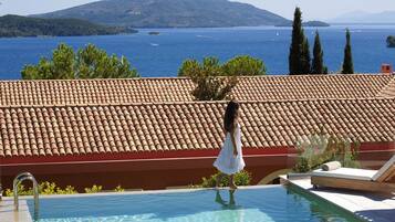 A swimming pool with a tiled roof, a view of the sea, and a person walking by.