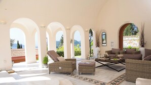 A spacious living area with a view of mountains, featuring wicker furniture, a marble floor, and a large window. - Villa Veneziano Lefkada (Lefkada)
