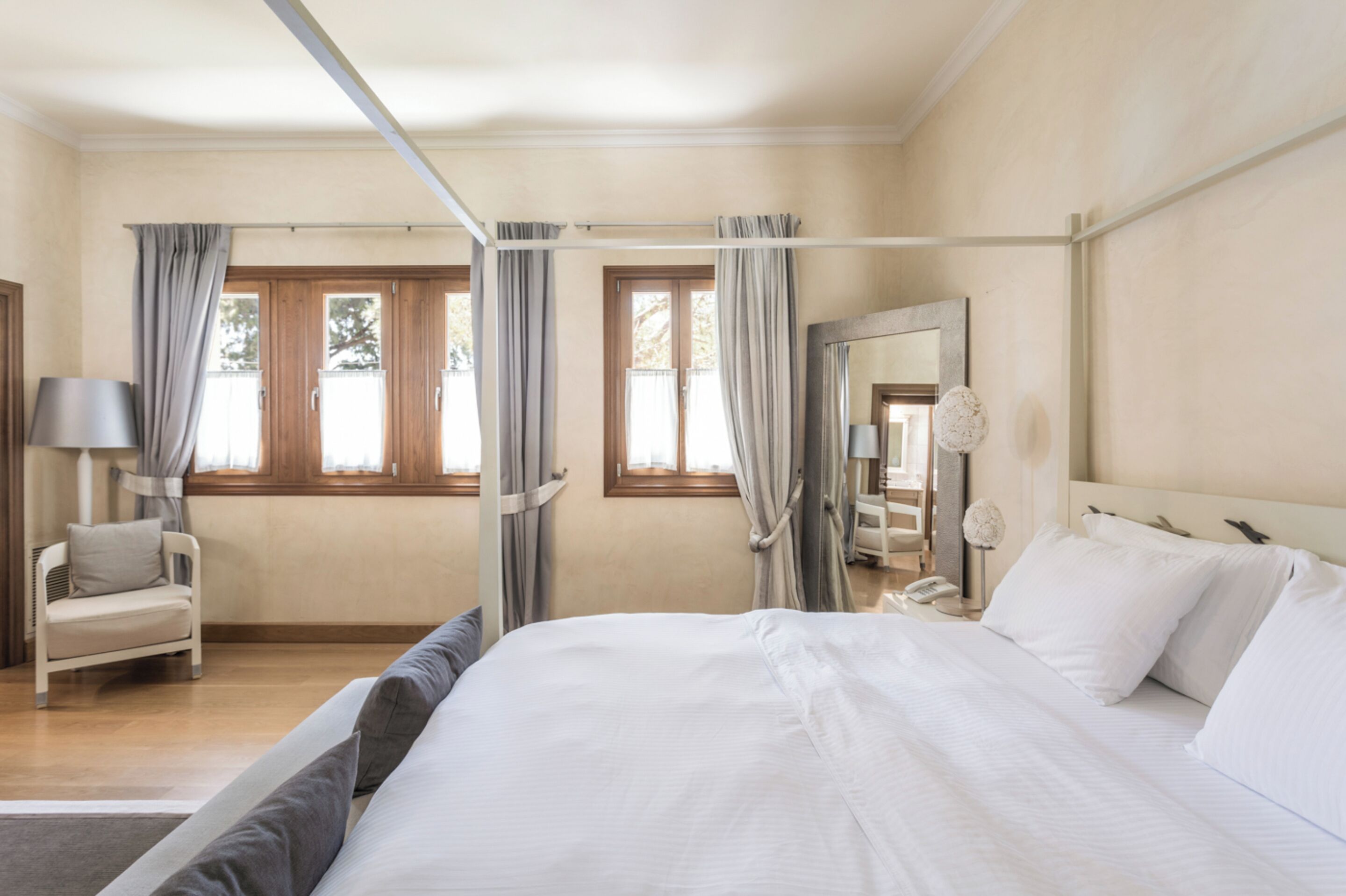 A hotel room with a large bed, a chair, a desk with a lamp, and a window with curtains.