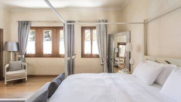 A hotel room with a large bed, a chair, a desk with a lamp, and a window with curtains.