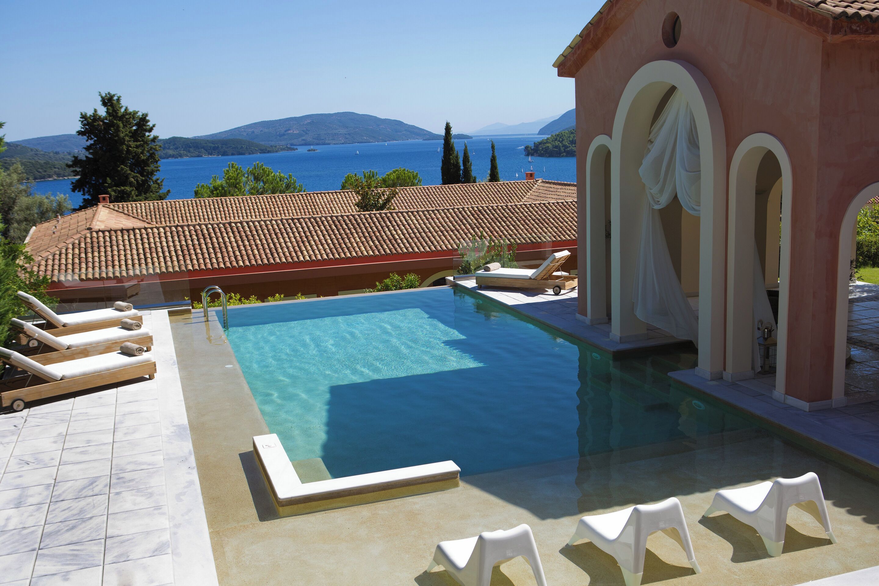 A swimming pool with clear blue water, surrounded by lounge chairs and a building with arches.