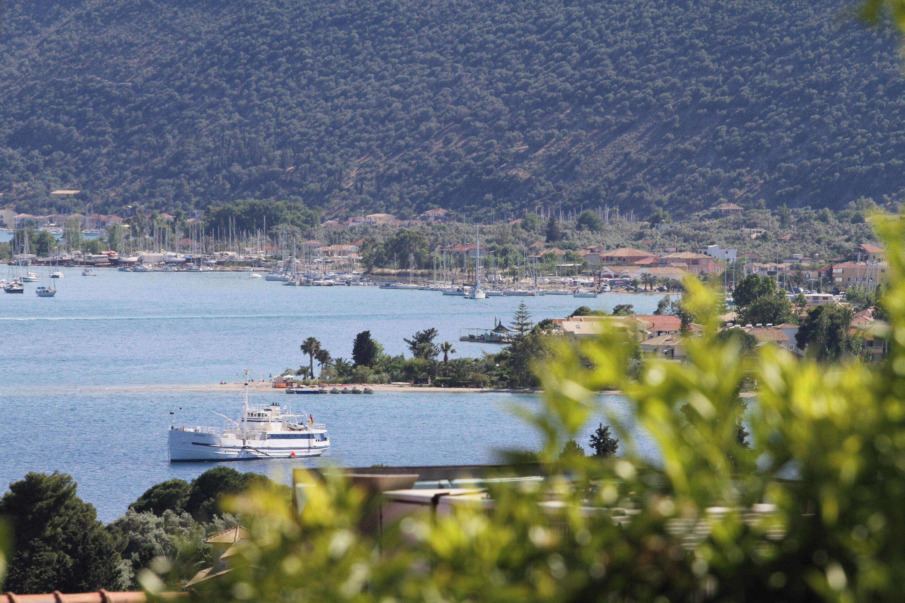 A coastal town with a marina, boats, and a hillside with buildings.