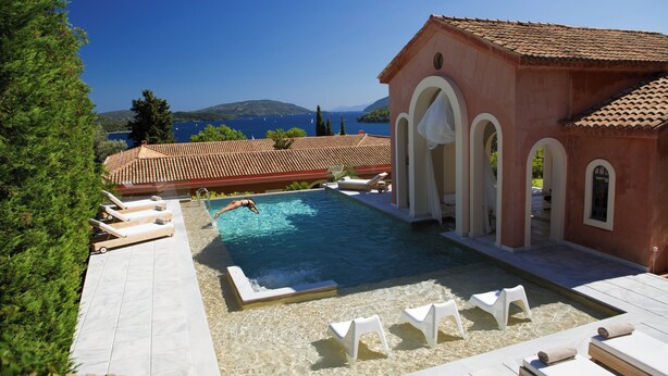 A swimming pool with lounge chairs, a building with arches, and a view of the sea. - Villa Veneziano Lefkada (Lefkada)
