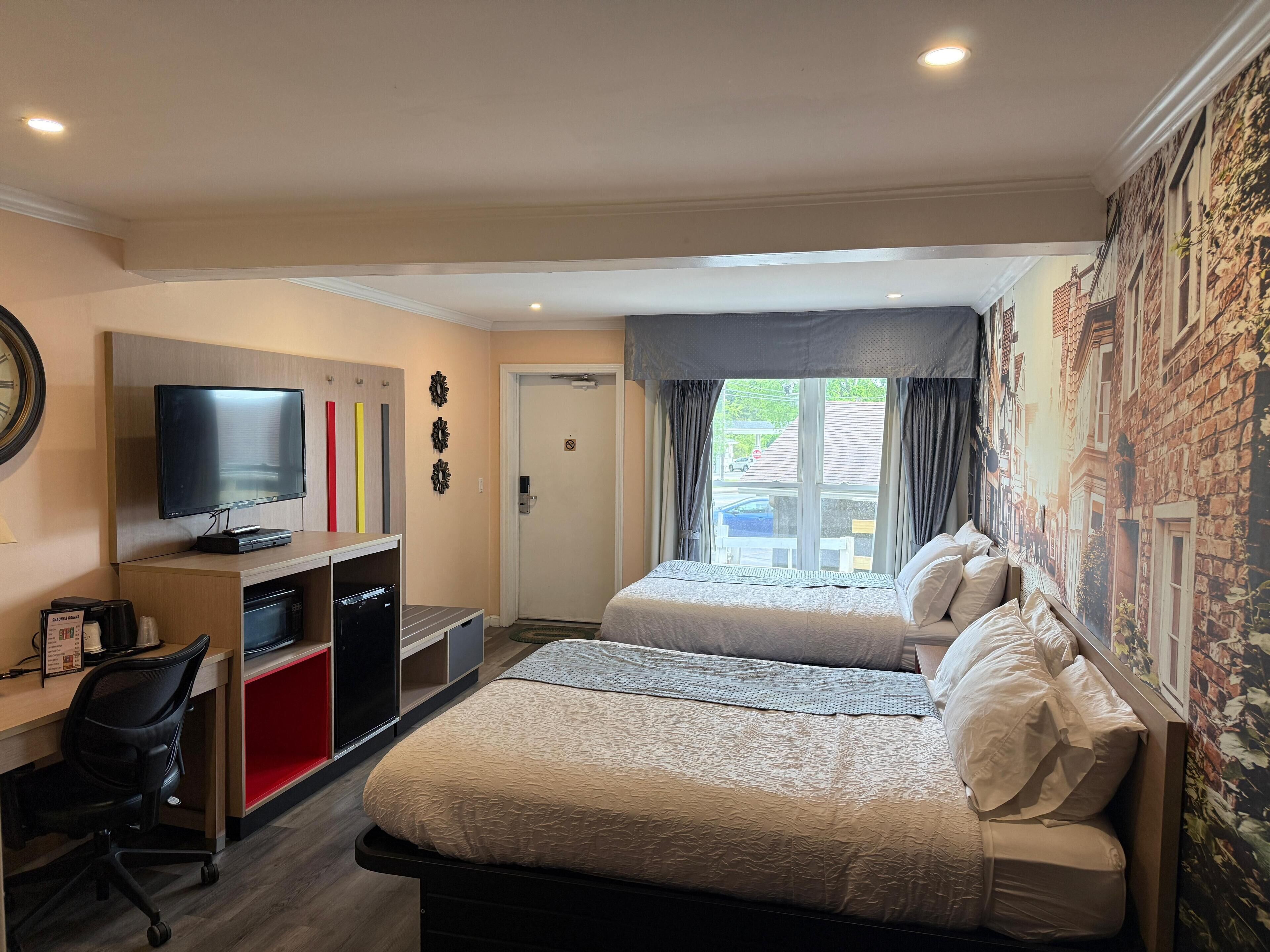 Habitación de hotel con una cama, un escritorio con computadora, televisor y ventana con vista a la calle.