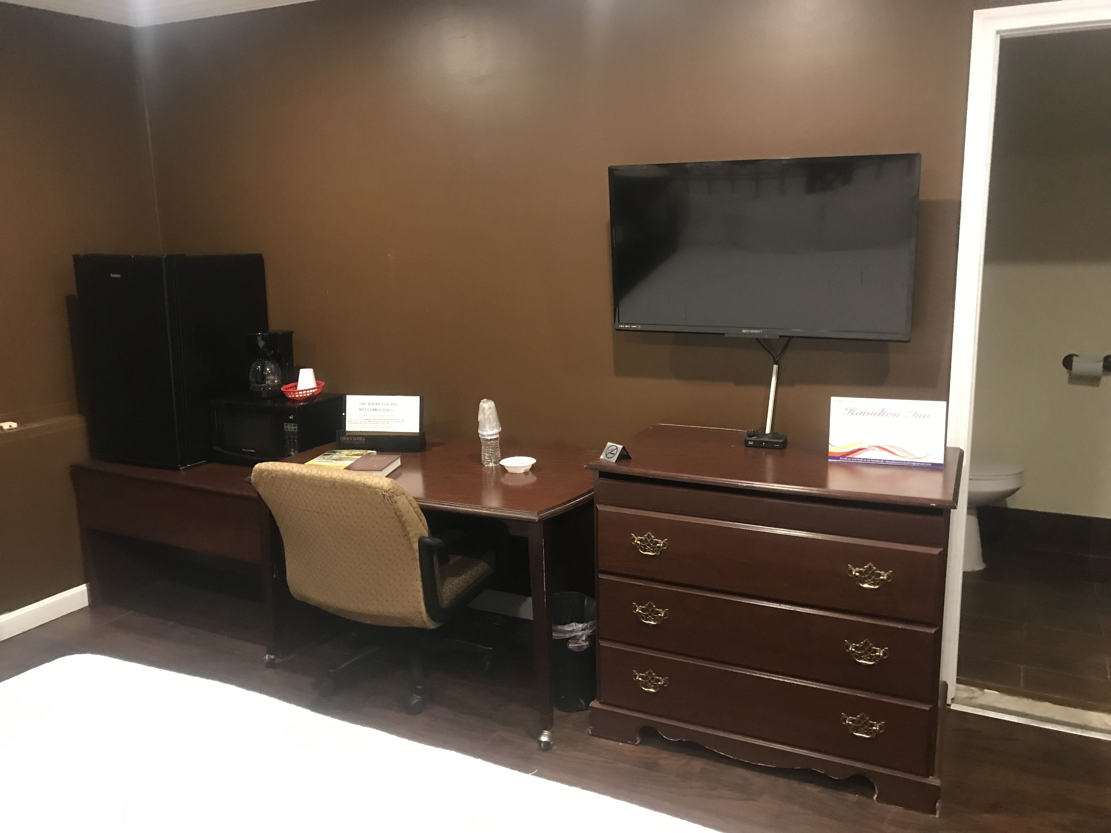 A hotel room with a desk, chair, television, and a minibar.