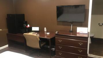 A hotel room with a desk, chair, television, and a minibar.