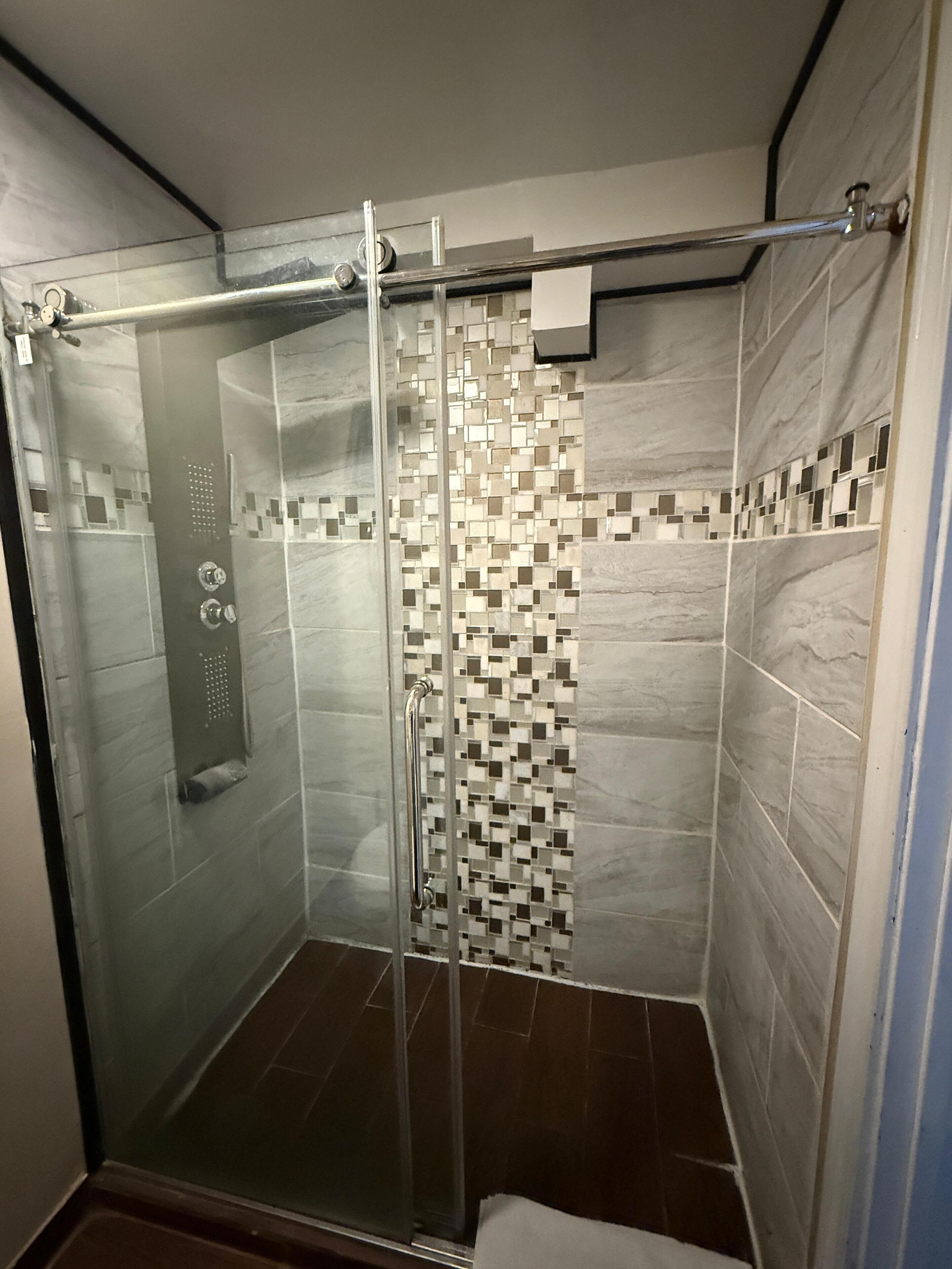 Una ducha con cerramiento de vidrio, pared de azulejos y una manija metálica.