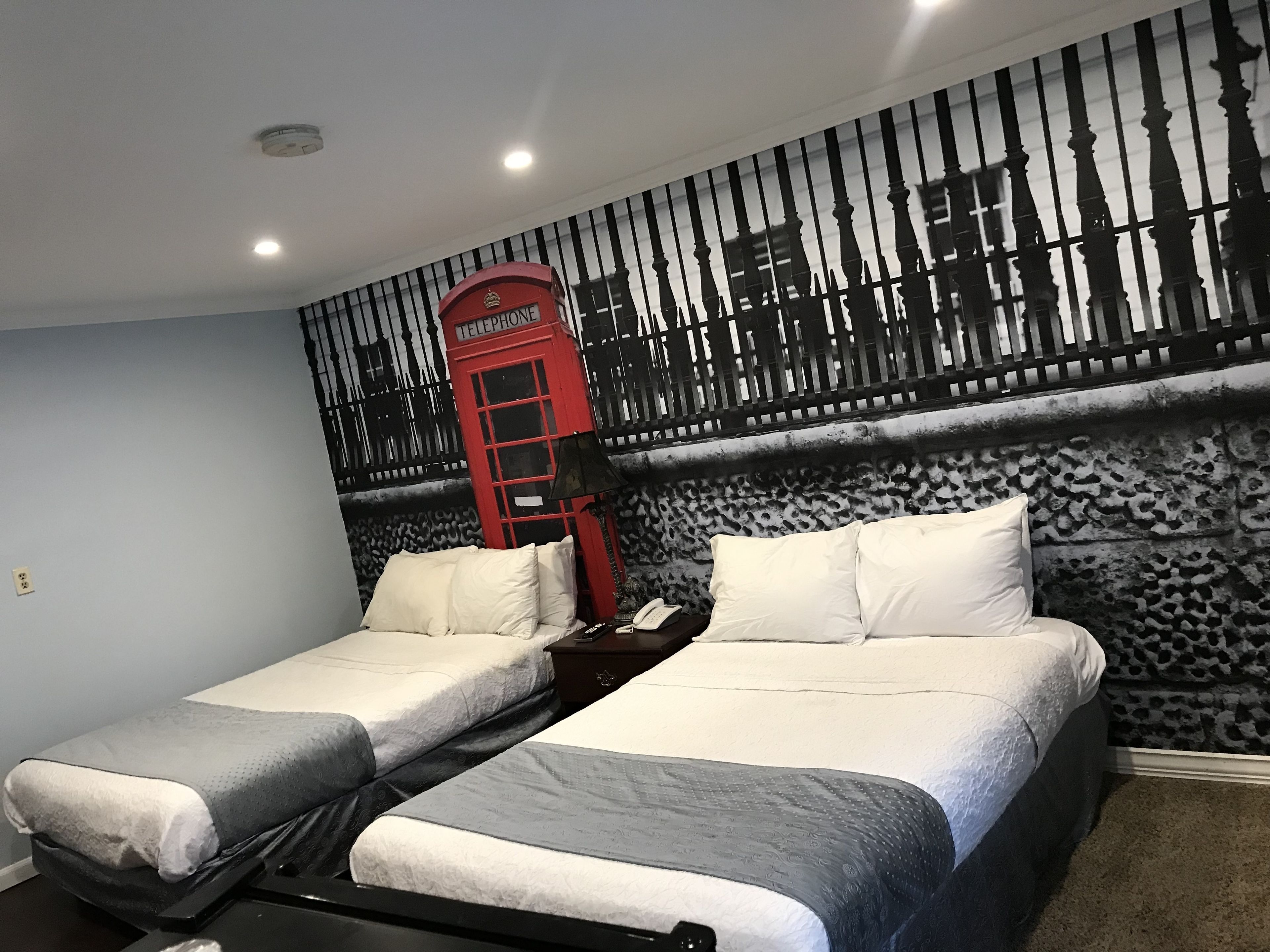 Una habitación con dos camas, un teléfono público rojo y un papel tapiz estampado.