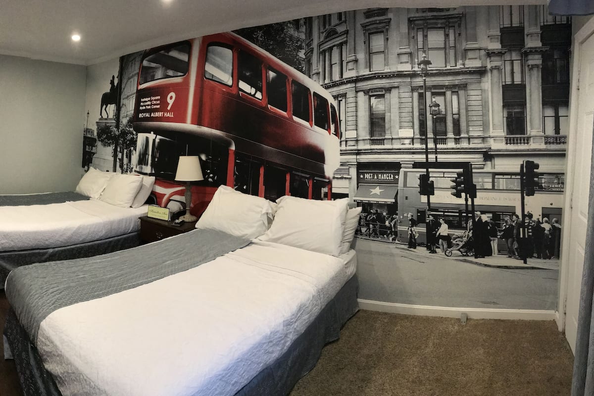 A hotel room with two single beds, a red double-decker bus mural, and a cityscape view.