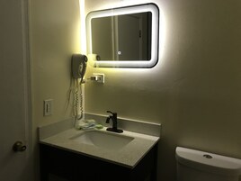 Un baño con lavamanos blanco, un espejo con luz, un secador de pelo y un inodoro.