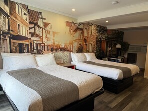 A hotel room with two beds, a mural of a street scene, and a small table with a lamp. - Hamilton Inn (Sturbridge)
