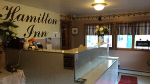 A reception area with a 'Hamilton Inn' sign, a reception desk, a 'Welcome' sign, and a window with curtains.