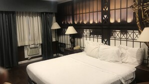 A hotel room with a large bed, two bedside lamps, a nightstand with a telephone, and a decorative headboard.